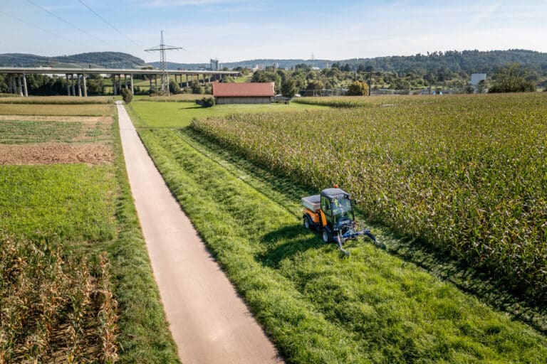 Karcher Holder C 70 Municipal tractor mowing greenery alongside a grain field