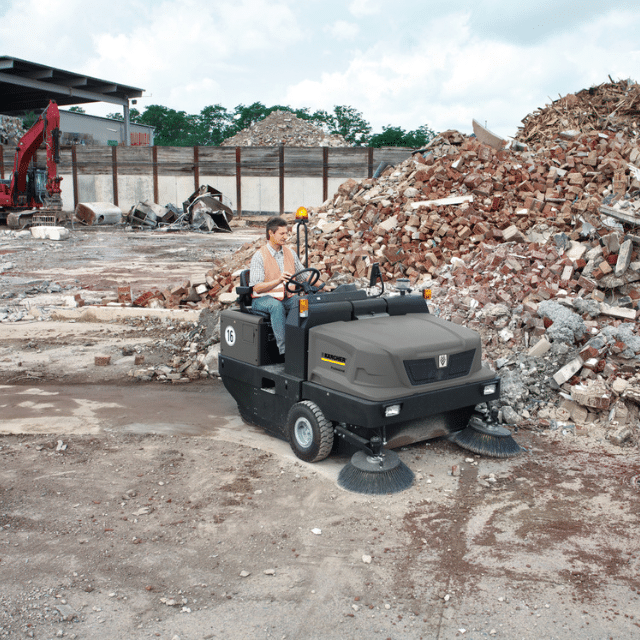 Karcher industrial ride on sweeper cleaning up a pile of discarded industrial materials